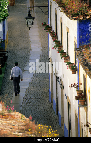 Europa, Portugal, Obidos. Mann zu Fuß in enge Gasse mit weiß getünchten Häusern mit Blumen geschmückt. Stockfoto