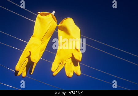 Nahaufnahme von ein paar hellen gelben Gummi, die Handschuhe gekoppelt, zum Trocknen auf der Wäscheleine unter tiefblauem Himmel Stockfoto