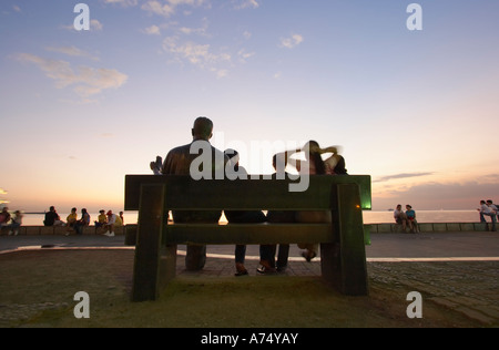 Leute sitzen auf Bank mit Statue In Manila Bay Stockfoto