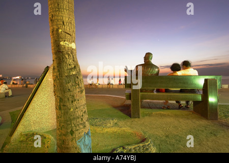 Leute sitzen auf Bank mit Statue In Manila Bay Stockfoto