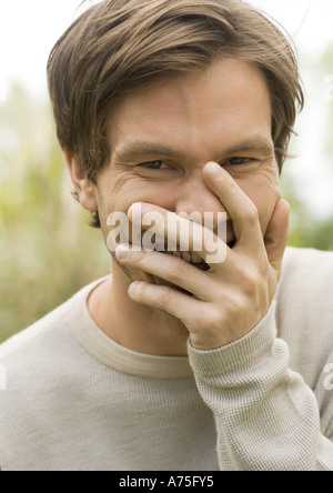 Junger Mann, lachend und den Mund mit der Hand, Porträt Stockfoto