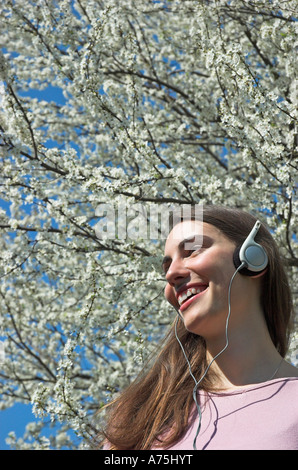 Junge Frau trägt Kopfhörer Frühjahr blühen im Hintergrund Stockfoto