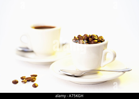 Zwei Espresso-Tassen, die man mit Kaffeebohnen gefüllt weißer Hintergrund Stockfoto