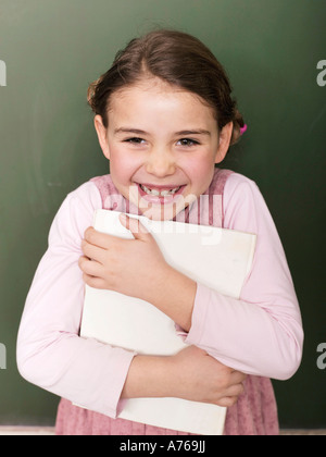 Mädchen (5-6) steht von Blackboard, Holding-Buch, portrait Stockfoto