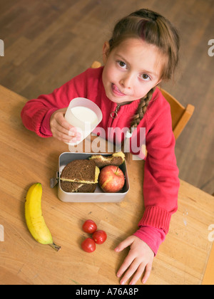 Mädchen (4-7) halten Glas Milch und Lunch Box von Schreibtisch, erhöhten Blick Stockfoto