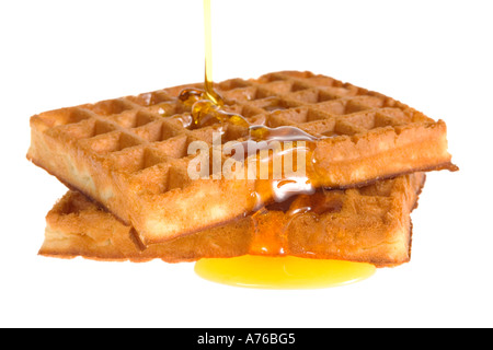 Ahornsirup ausgegossen über zwei heiße Waffeln auf einem reinen weißen Hintergrund. Stockfoto