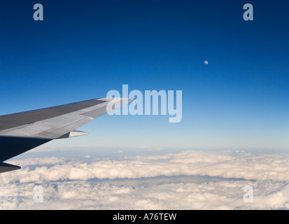 Luftaufnahme, Blick hinunter auf weißen Wolken fliegen über sie in großer Höhe mit Flugzeugen Flügelspitze gegen blauen Himmel und Vollmond Stockfoto