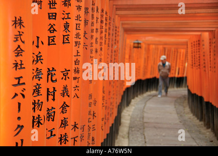 Orange lackiert Torii-Tore im Fushimi Inari-Taisha-Schrein in Kyoto Japan Kanji geschrieben Beiträge Walkng Mann im Bokeh jenseits Stockfoto