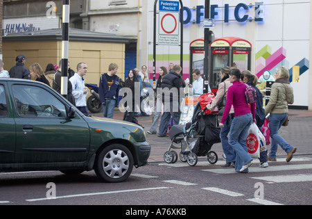 Käufer und Familien überqueren die Fußgängerüberführung vor dem angefahrensten Auto, während sie an Heiligabend in Belfast einkaufen Stockfoto