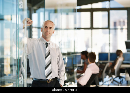 Geschäftsmann, stützte sich auf Tür im Büro, mit Büroangestellte im Hintergrund. Stockfoto