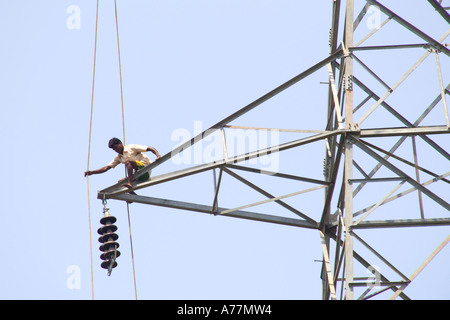 Eine indische Arbeiter, die hoch oben auf einen Strommast installieren neue Kabel mit keine Sicherheitsseile balancieren. Stockfoto