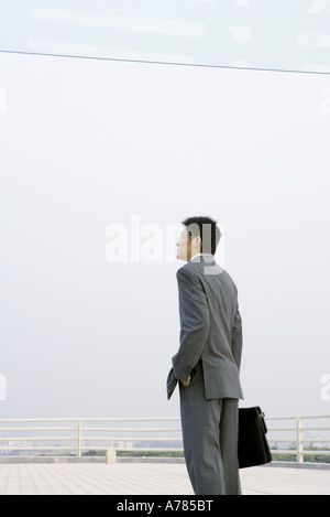 Geschäftsmann mit Aktenkoffer auf Bürogebäude Terrasse stehend Stockfoto