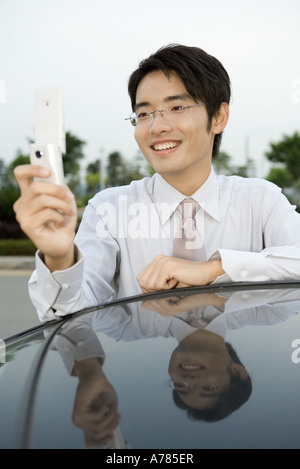 Junger Geschäftsmann gelehnt Auto, Handy, hält lächelnd Stockfoto