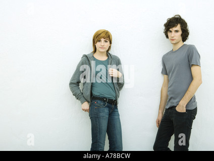 Junger Mann und junge Frau Wand gelehnt, Blick in die Kamera, weißer Hintergrund Stockfoto