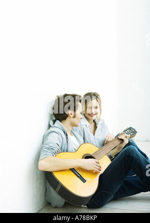 Junges Paar sitzt am Boden, Mann spielt Gitarre Stockfoto