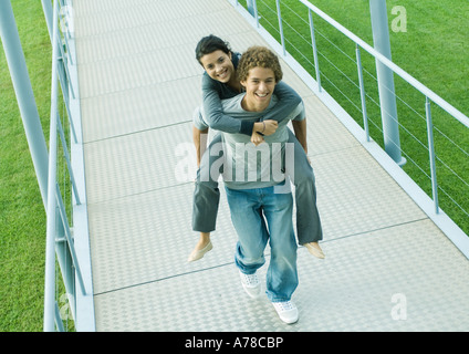 Teenager-Paar, junge Mädchen tragen Huckepack auf Gehweg, lächelnd in die Kamera Stockfoto