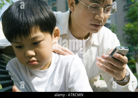 Mann, Blick auf Handy, während Sohn entfernt, blickt finster Stockfoto