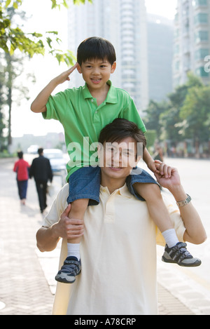 Junge Reiten auf Vaters Schultern, salutieren, Kamera Stockfoto