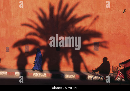 Schatten von Palmen und Menschen auf ockerfarbenen Wänden, am frühen Abend in der Marrakech Street, Marokko Stockfoto