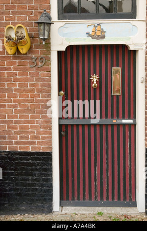 Eintritt zu einem kleinen typisch holländischen Backsteinhaus in Edam mit Holzschuhen, Nordholland. Verfügt über eine gestreifte Tür und gelbe Clogs an einer Ziegelwand. Stockfoto