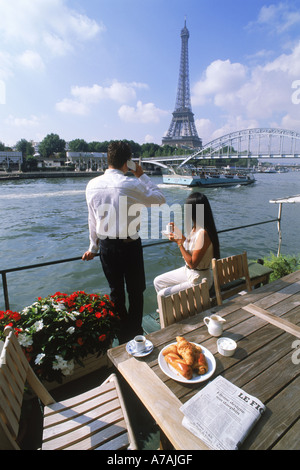 Paar am Ufer Hausboot gegenüber dem Eiffelturm mit Kaffee, Croissants und Handy Stockfoto