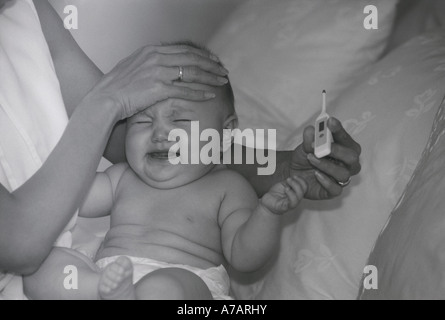 Mutter hielt schreiendes Baby mit Feavor kleinen Thermometer Temperatur mitnehmen Stockfoto