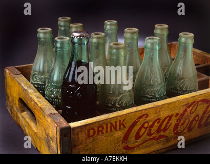 Eine volle Flasche und eine Gruppe leere Flaschen. Vintage Coca Cola Flaschen im Holzkoffer Stockfoto