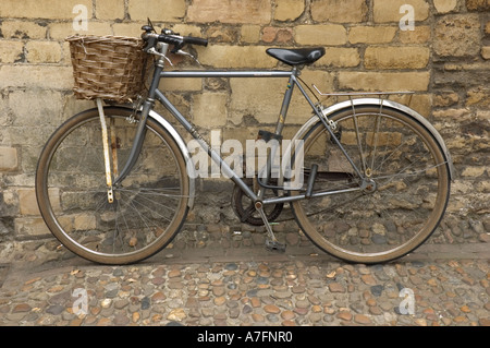 Altes Fahrrad mit Weidenkorb gegen alte gelbe Steinmauer des University College, Cambridge, England, Großbritannien Stockfoto