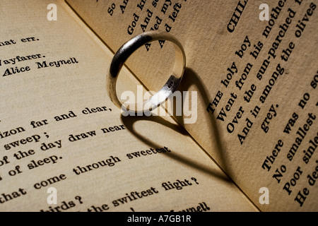 Ehering wirft einen herzförmigen Schatten auf ein Buch mit Gedichten Stockfoto