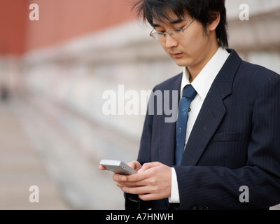 Ein junger Chinese Business Mann in einem Anzug überprüft seine Telefon Stockfoto