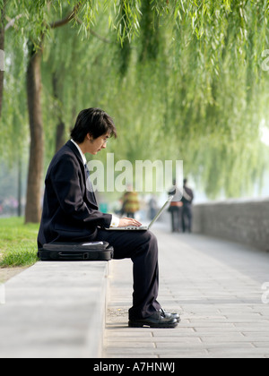 Junge chinesische Geschäftsmann im Anzug seine e-Mails auf seinem laptop Stockfoto