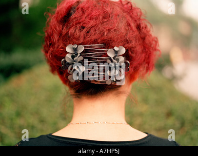 Ein Porträt von einer chinesischen Frau s Hinterkopf mit leuchtend roten Haaren und großen Clips halten es auf dem Platz in einem park Stockfoto