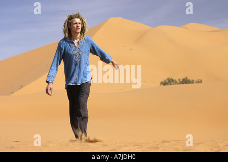 Junger Mann mit blonden Dreadlocks gehen in der Wüste an einem sonnigen Tag Stockfoto