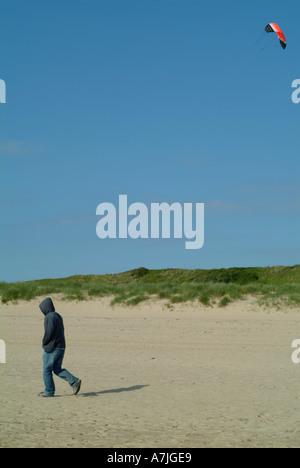 Drachen steigen lassen und Mann zu Fuß am Strand von Rock Cornwall England Uk Stockfoto