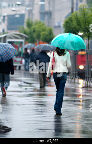 Junge Frau zu Fuß entlang einer belebten Straße der Stadt im Regen Stockfoto
