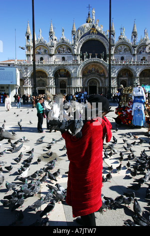 Ältere Frau im roten Mantel füttert Tauben auf dem Arm vor St. Marks Basilica Kathedrale zentrale Venedig Italien Europa EU Stockfoto