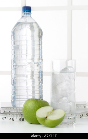 PORTRÄTAUFNAHME VON EINE FLASCHE WASSER MIT EINEM GLAS WASSER UND EINEM GANZEN ZWEI ÄPFEL UND EIN SCHNITT IN DER MITTE MIT MAßBAND Stockfoto