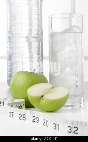 PORTRÄTAUFNAHME VON EINE FLASCHE WASSER MIT EINEM GLAS WASSER UND EINEM GANZEN ZWEI ÄPFEL UND EIN SCHNITT IN DER MITTE MIT MAßBAND Stockfoto