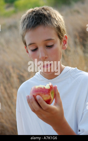 junge isst Apple auf einer Wiese außerhalb Stockfoto