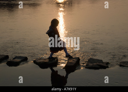 Trittsteine - ein junges Mädchen, die Überquerung eines Flusses in der Abenddämmerung. Stockfoto