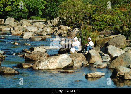 Afon Glaslyn Fluss in der Nähe von Beddgelert in Aberglaslyn Pass Nahaufnahme Menschen sitzen auf Felsen entspannen malerische walisische Landschaft Snowdonia Gwynedd, Nordwales Stockfoto