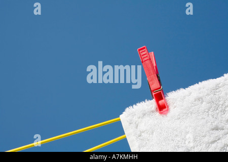 Wäscheklammer auf ein weißes Handtuch und Wäscheleine vor blauem Himmel Stockfoto