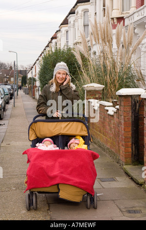 Mutter mit Mobiltelefon und schieben Kinderwagen, London, England Stockfoto