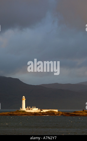 Leuchtturm auf Eilean Musdile in der Sound Mull westlichen Inseln Schottlands im morgendlichen Sonnenlicht mit dunklen, stürmischen Wolken Stockfoto