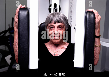 Eine lächelnde senior Frau im schwarzen Trikot trainieren ihre Arme auf einer PecDec Maschine Stockfoto