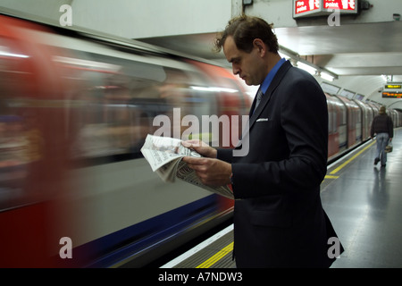 Stadt Gent Zeitungslektüre auf der Londoner U-Bahn Station mit Zug nähert sich England-Großbritannien Stockfoto