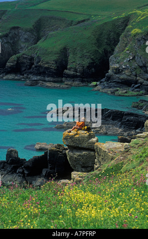 Weibliche Walker sitzt auf einem Felsen bewundern die Aussicht auf Housel Bucht an einem schönen sonnigen Tag The Lizard Cornwall England Stockfoto