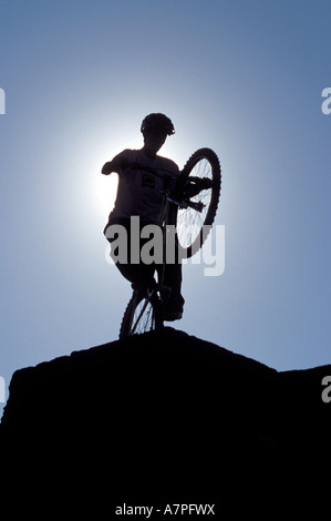 Mountainbiker gegen die Sonne machen einen Wheelie auf einer Wand Cornwall UK Stockfoto