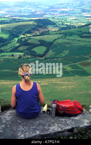 Einsame weibliche Walker in den Brecon Beacons erholend auf einem Felsen und mit Blick über das Tal. Stockfoto