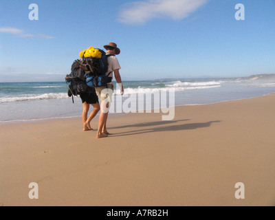 Zwei Wanderer gehen barfuß mit Rucksäcken am Strand während der Strandloper Wandern trail Cintsa Eastern Cape Stockfoto